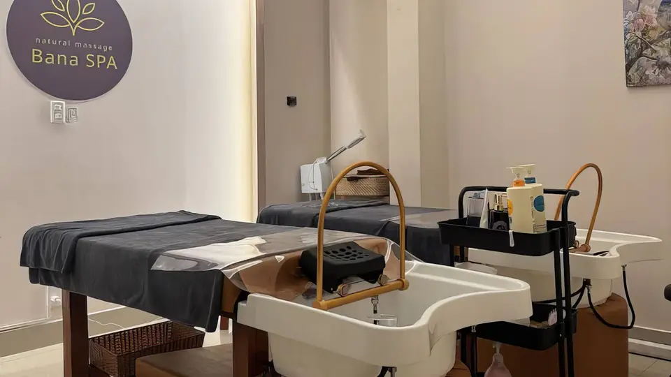 バナスパのロゴが壁面に掲げられたルーム内の2台のマッサージベッドとヘアシャンプー台、ケア用品カート