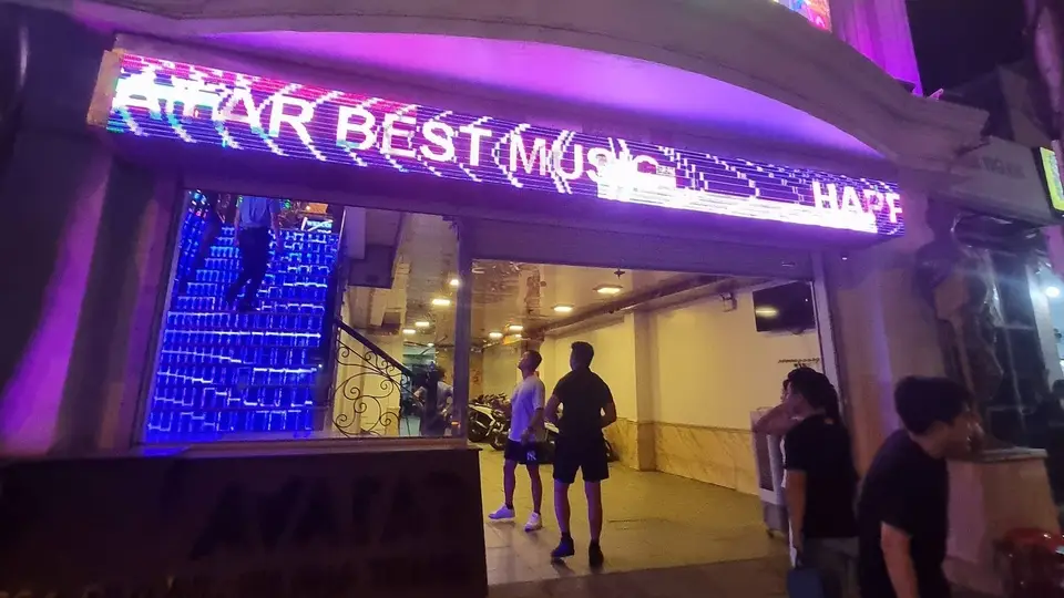 Nighttime exterior of Avatar Karaoke featuring purple neon signs and blue LED panel staircase