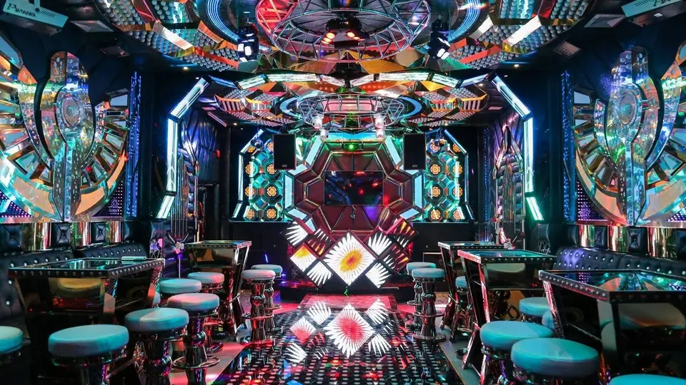 Crown Karaoke private room interior with faceted mirror panel ceiling, colorful LED lighting, and circular bar table