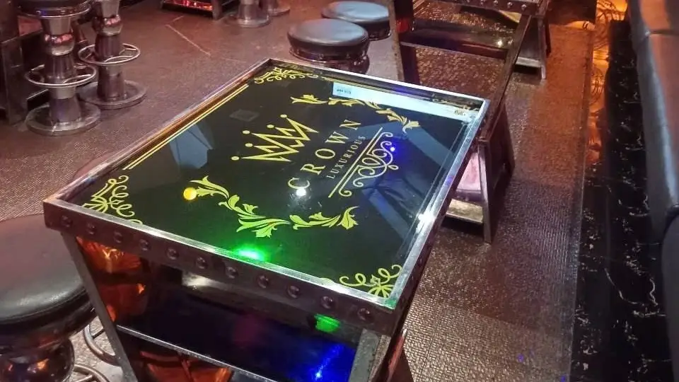 Crown Karaoke in-room service table with mirror surface engraved with CROWN logo and crown motif, alongside leather stools