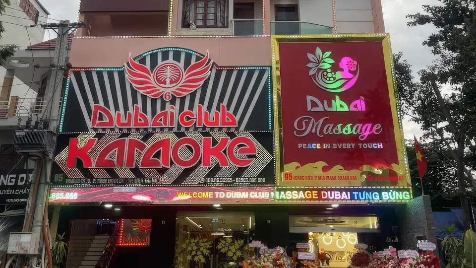 Full exterior view of Dubai Karaoke with red wing logo and neon signage on a striped pattern facade