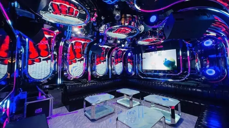 Dubai Karaoke dark room with red floral-patterned mirror walls, black leather sofas, and a glass table
