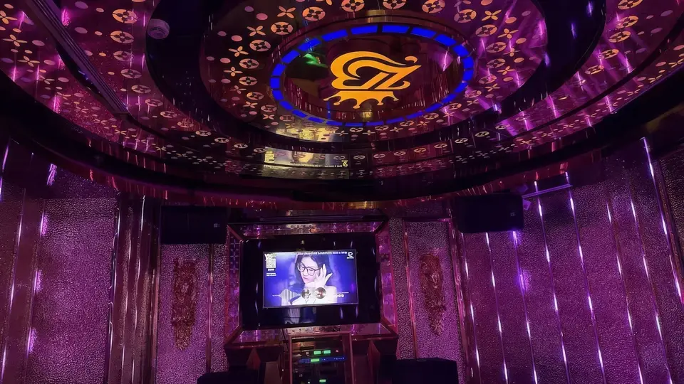 ゴールドパターンの天井にブルーネオンリング照明とブランドエンブレムが映え、大型LEDテレビが設置されたリバティ カラオケのプライベートルーム内部
