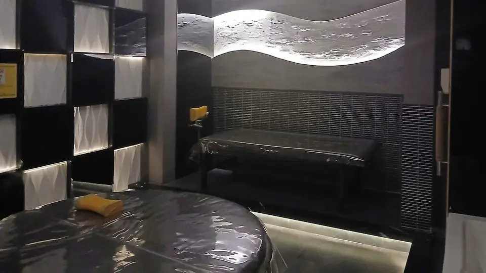 Interior of a luxury spa room with wave-shaped backlit panels, black tiles, and two massage beds
