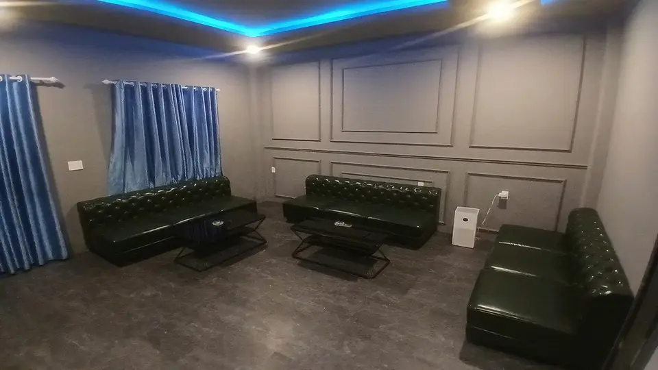 Spacious VIP lounge with blue ambient lighting and three dark green Chesterfield sofas