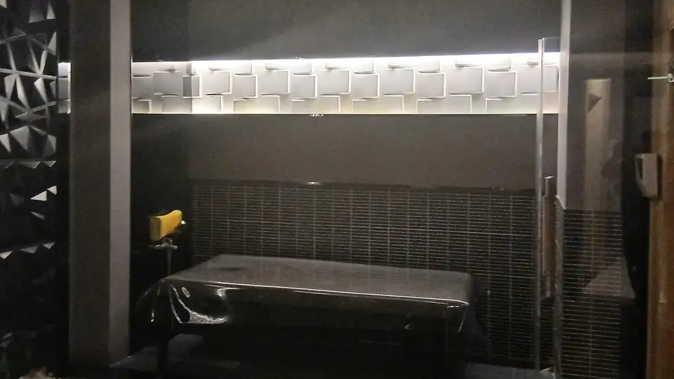 Dark-toned therapy room featuring white cube-patterned lighting, glass partitions, and a black massage bed