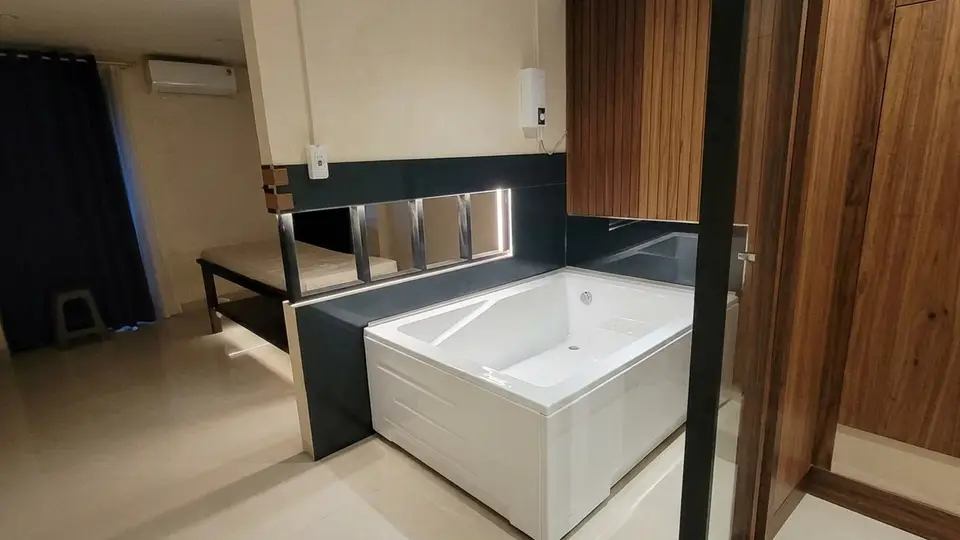 Interior of a spa room finished with dark tiles and wood panels, featuring a large white bathtub and a massage bed