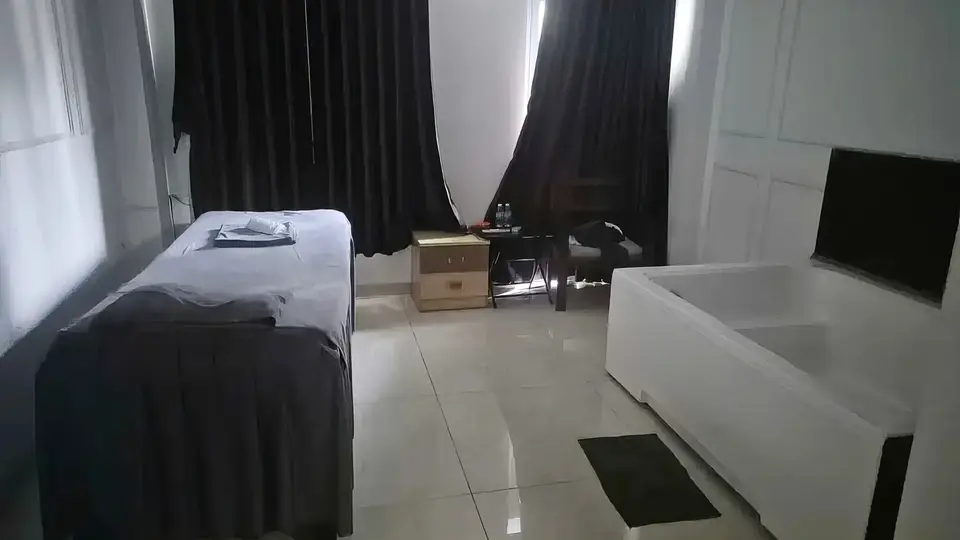 Deluxe room harmonizing black curtains and white interior, equipped with a massage bed, large bathtub, and wall-mounted TV