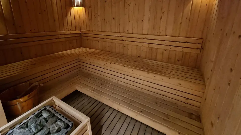 Interior of the Finnish dry sauna finished with natural pine panels, featuring a sauna stone heater and wooden water bucket